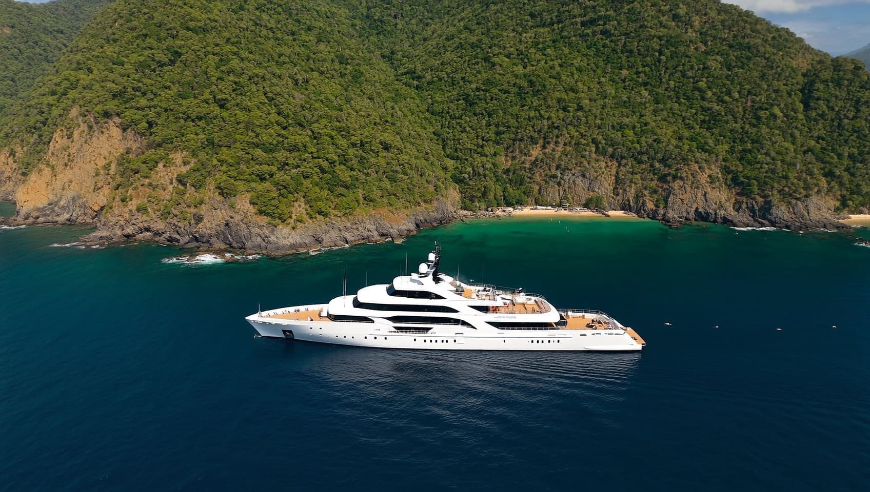 Aerial view of a yacht at anchor in a sheltered cove beneath forested cliffs