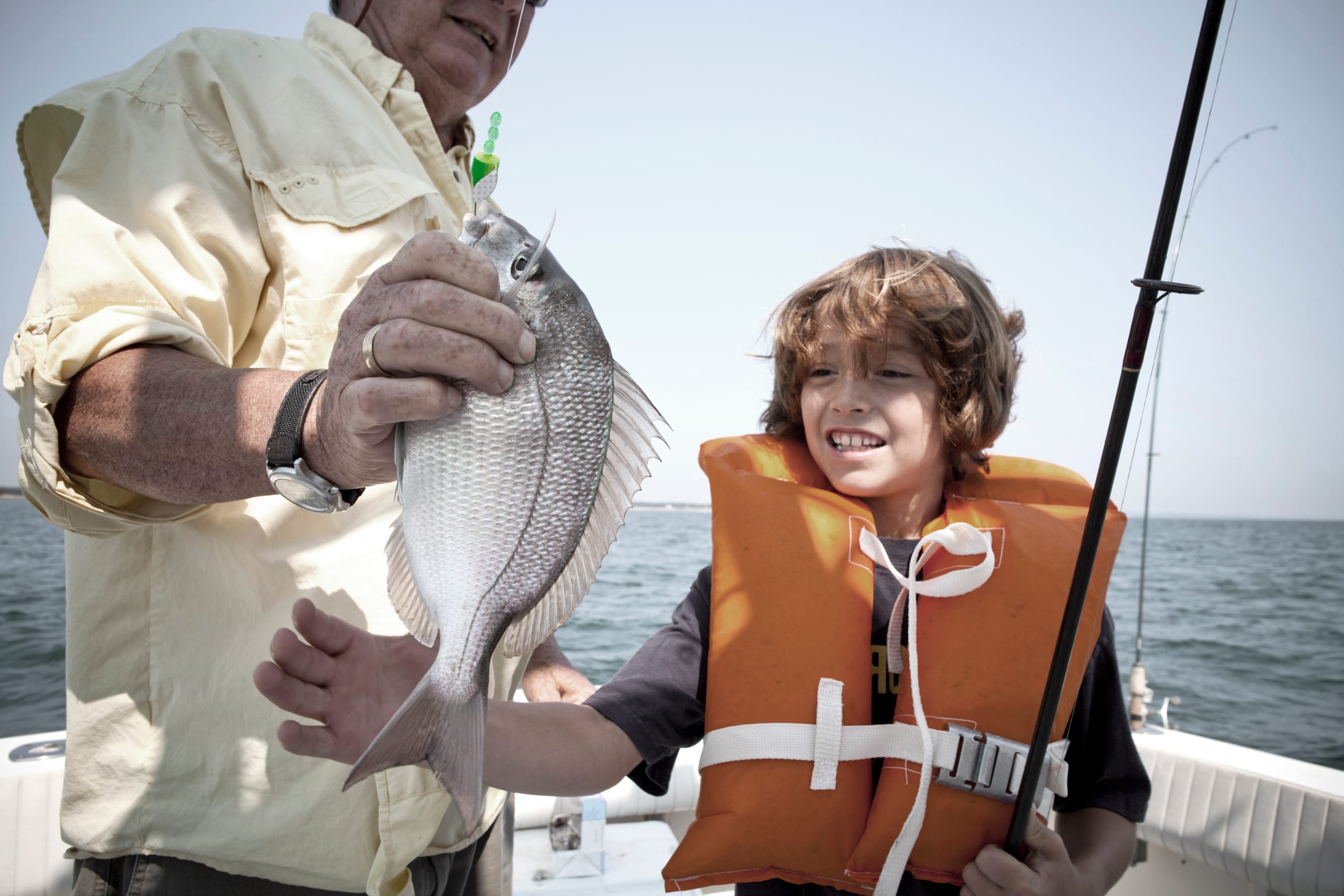 A young angler in a life jacket admiring the day's catch beside his guide