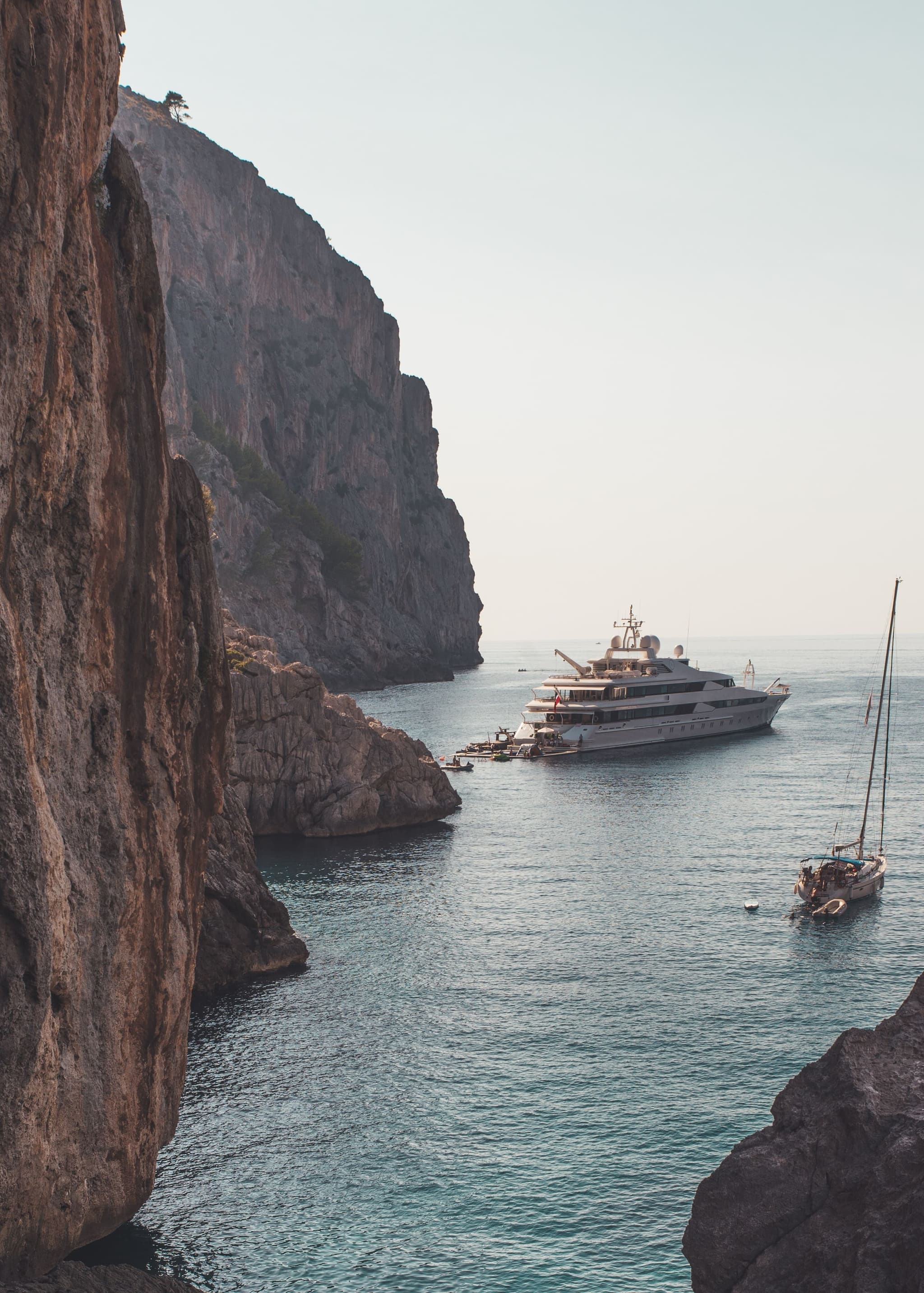 A superyacht at anchor in a sheltered cove beneath towering cliffs